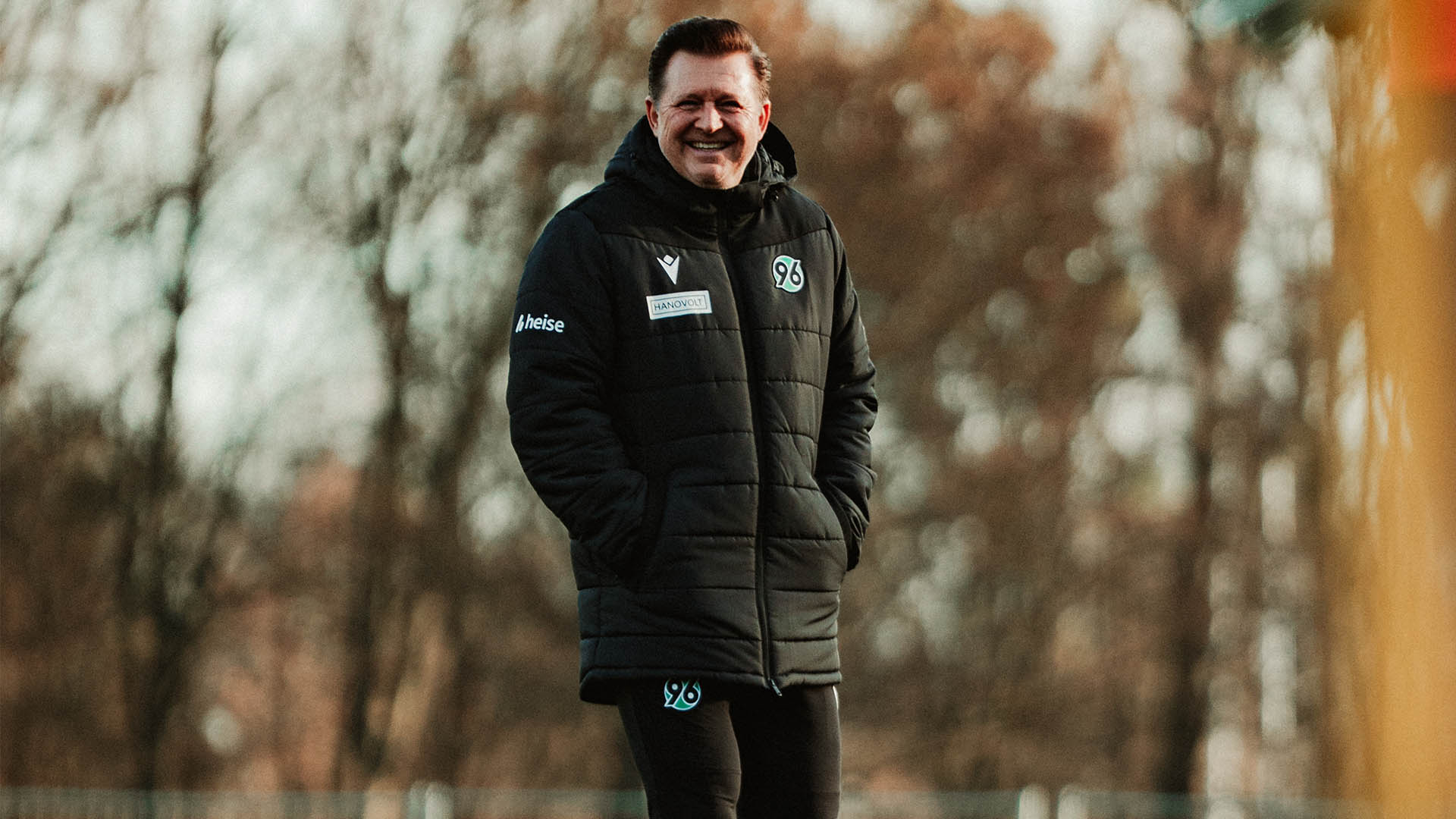 Christian Titz lächelnd mit Händen in den Taschen auf dem Trainingsplatz.