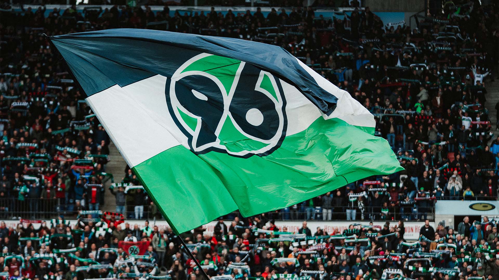 Eine große 96-Fahne wird im Stadion geschwenkt, im Hintergrund volle Ränge.