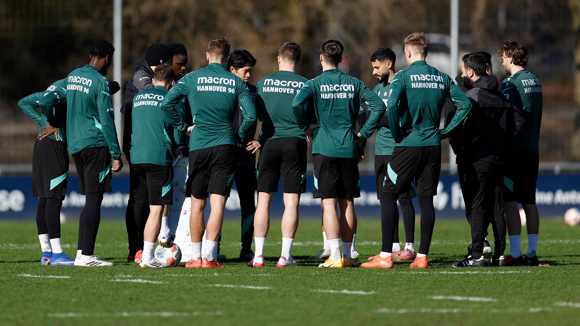 Ein Teil der Mannschaft steht in eine Kreis auf dem Trainingsplatz, die Sonne scheint.
