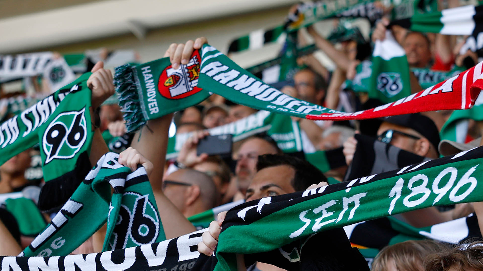 96-Fans halten Schals hoch, Gesichter sind nicht zu erkennen.