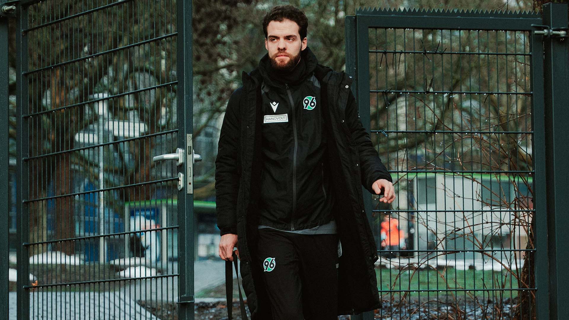 Der neue Videoanalyst betritt den Trainingsplatz in dicken Sachen, in der Hand trägt er eine kleine Tasche.
