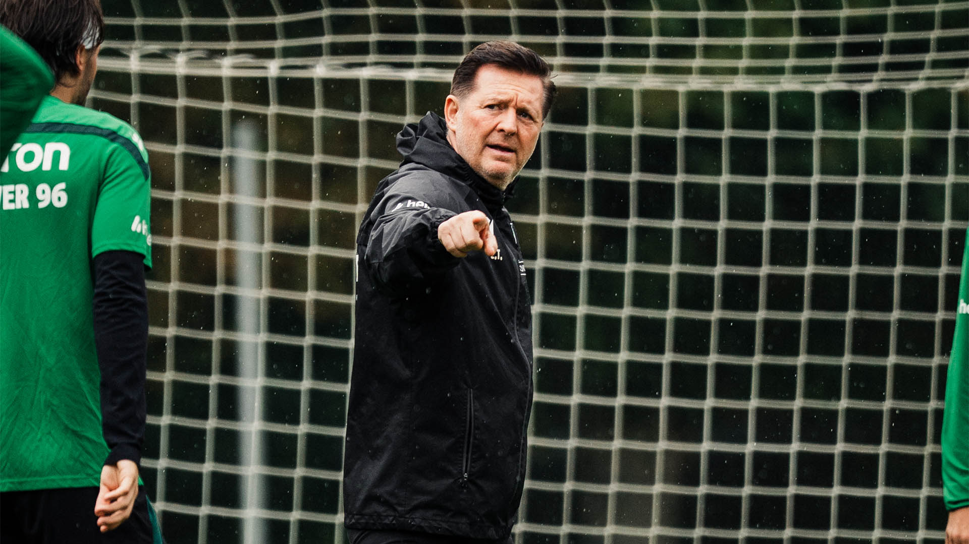 96-Cheftrainer Christian Titz steht auf dem Trainingsplatz und zeigt mit dem rechten Zeigefinger.