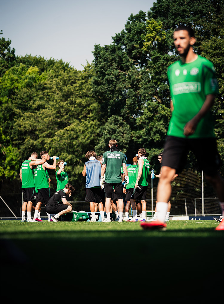 Ein Gruppe Spieler steht im Kreis auf dem Trainingsplatz und pausiert, einige trinken etwas. 