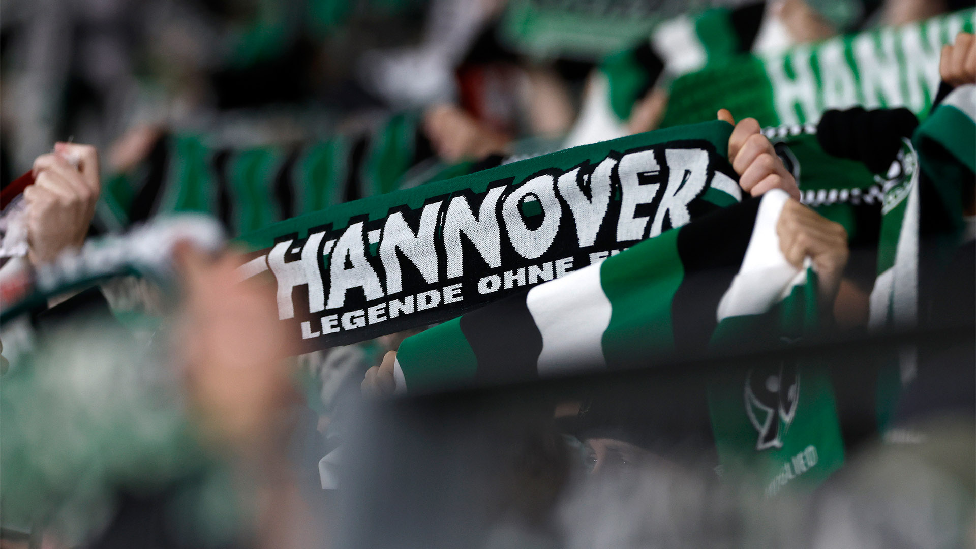Nicht erkennbare 96-Fans halten 96-Schals hoch.
