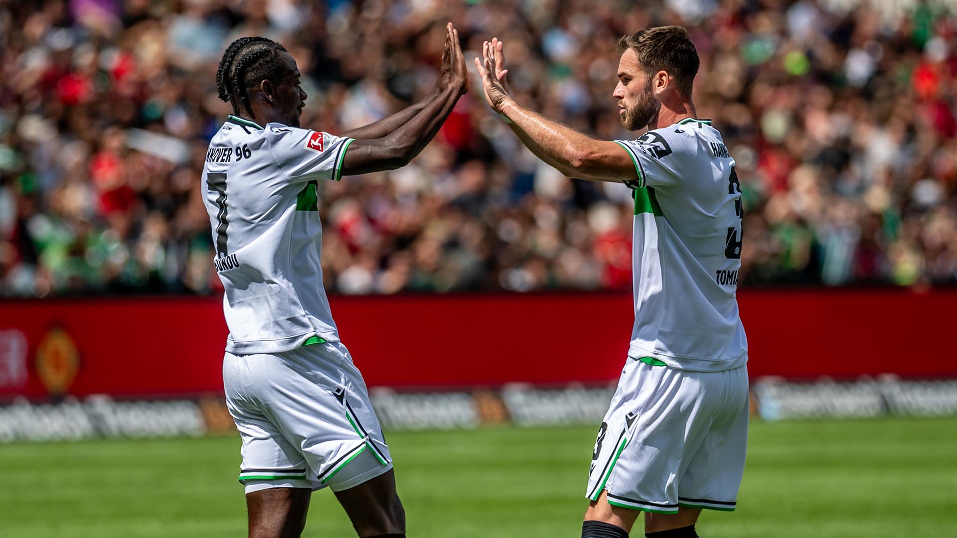 Mustapha Bundu und Boris Tomiak klatschen mit beiden Händen ab, im Hintergrund ist das volle Stadion.