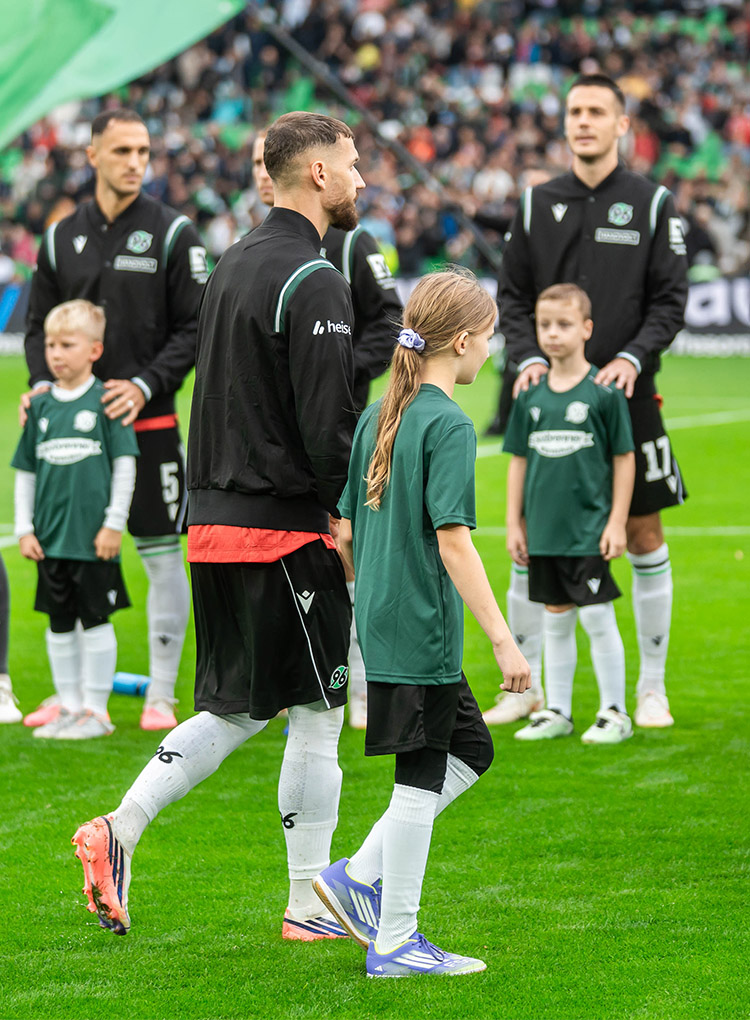 Einige 96-Spieler laufen mit Kids an der Hand ins 96-Stadion ein.