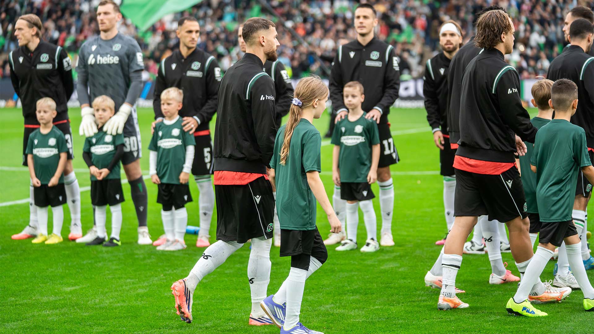 Einige 96-Spieler laufen mit Kids an der Hand ins 96-Stadion ein.