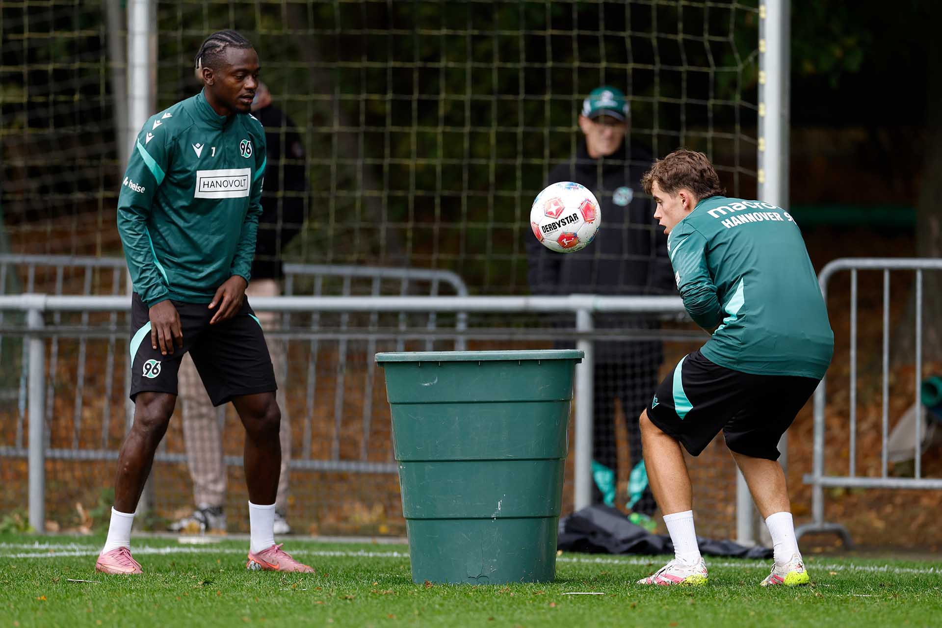 Mustapha Bundu steht vor einer Tonne, in die ein Nachwuchsspieler einen Ball köpft.