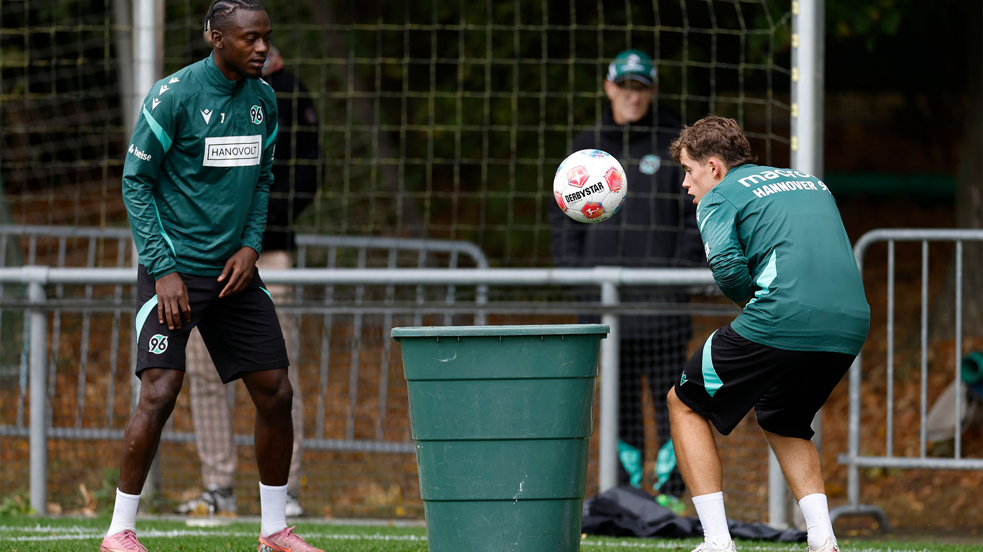 Mustapha Bundu steht vor einer Tonne, in die ein Nachwuchsspieler einen Ball köpft.