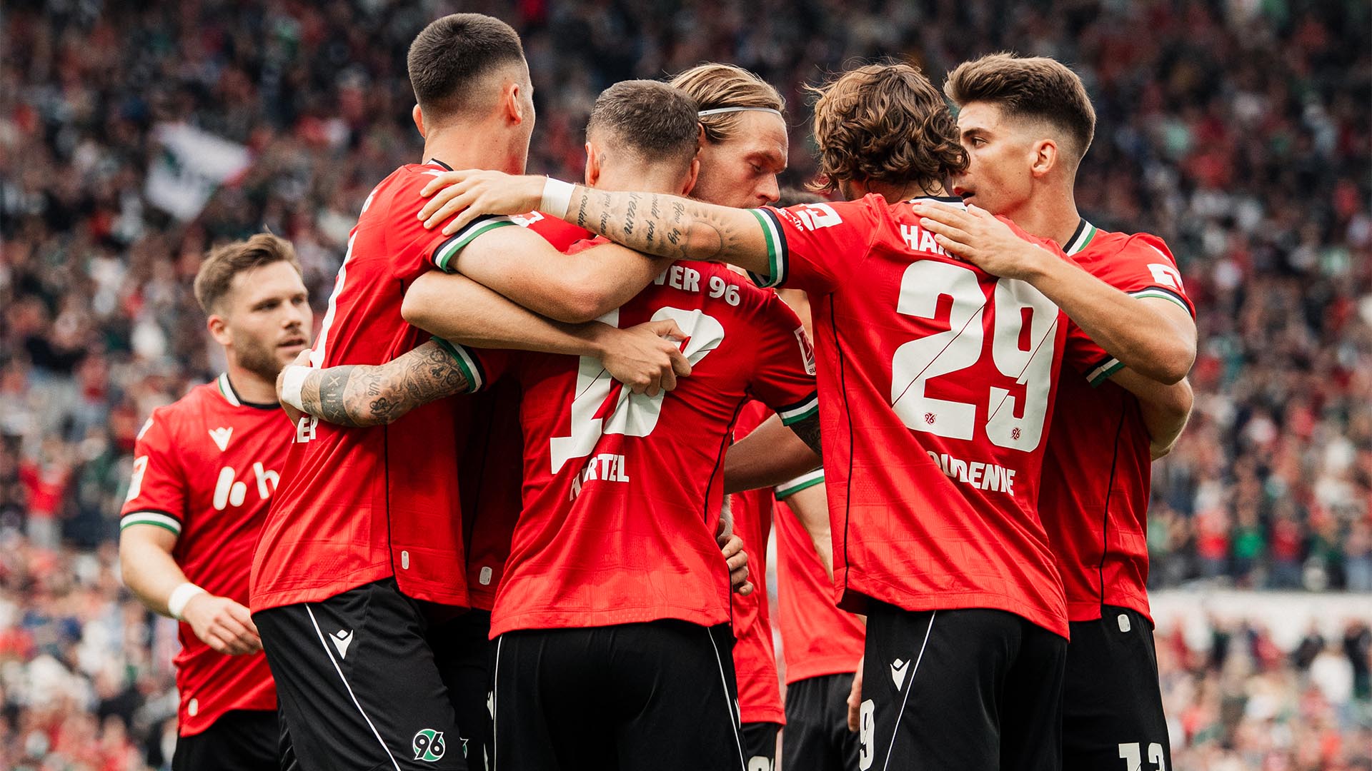 Eine Traube 96-Spieler jubelt im Heimstadion, im Hintergrund unscharf Fans.