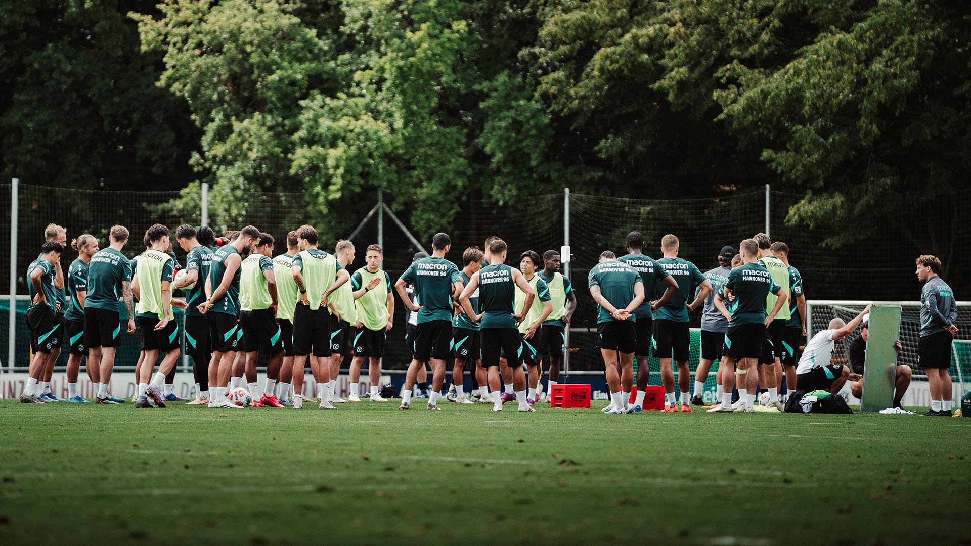 Die Mannschaft steht im Kreis auf dem Platz, das Trainerteam erklärt etwas an der Taktiktafel.