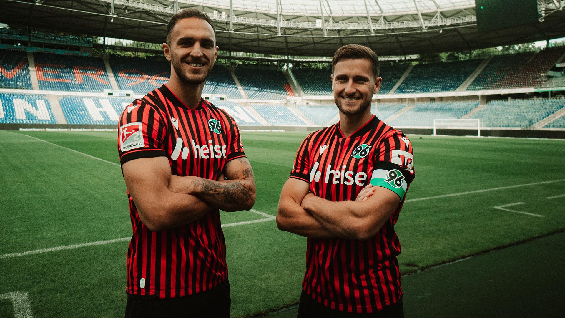 Virgil Ghita und Enzo Leopold stehen mit verschränkten Armen im Stadion, Leopold trägt die Kapitänsbinde. 