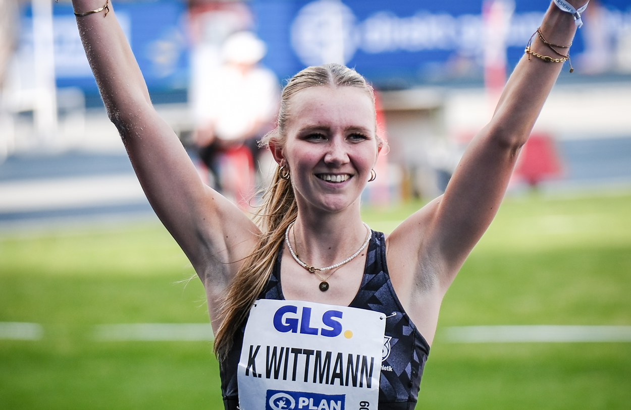 Kira Wittmann lächelt in die Kamera und hebt ihre Arme hoch.