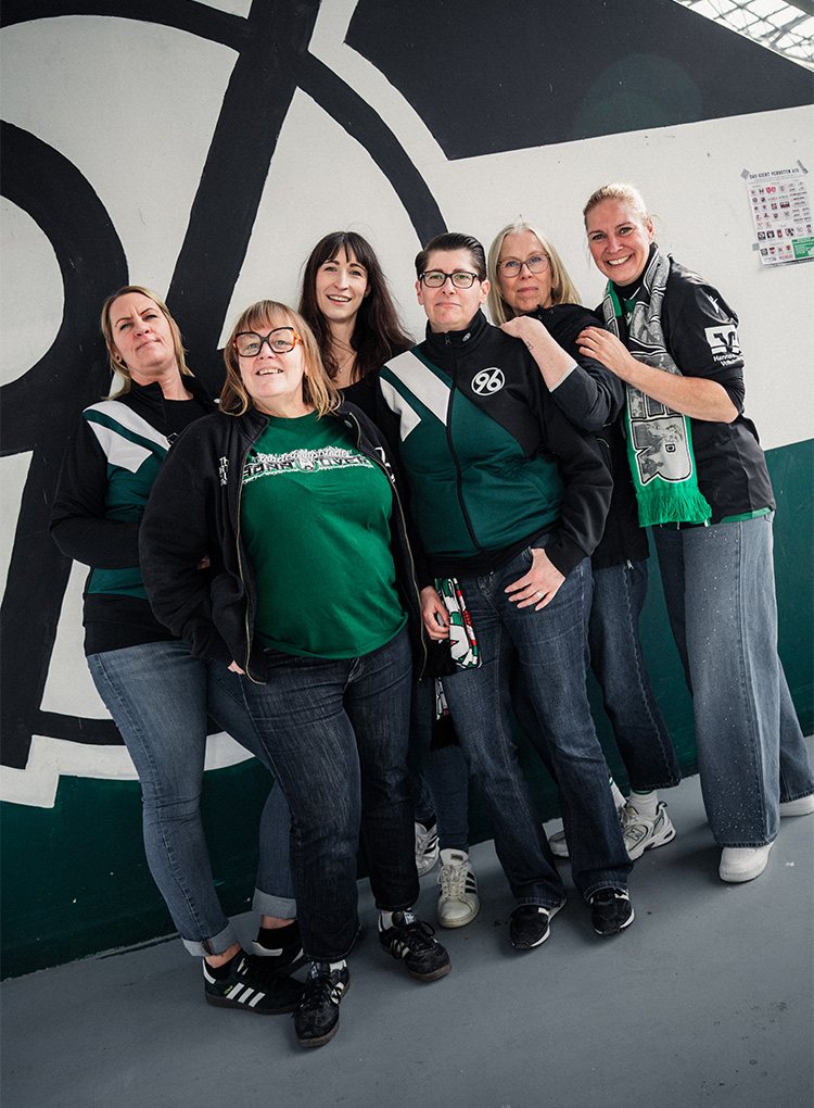 Sechs Frauen in 96-Klamotten stehen vor einem großen 96-Logo. 