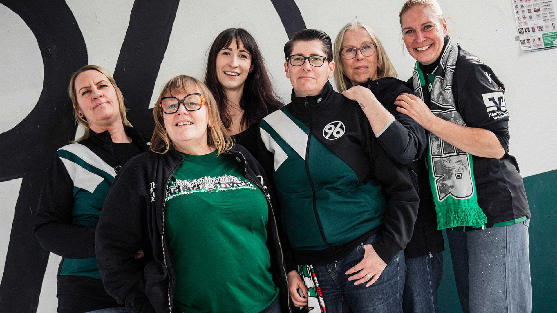 Sechs Frauen in 96-Klamotten stehen vor einem großen 96-Logo. 