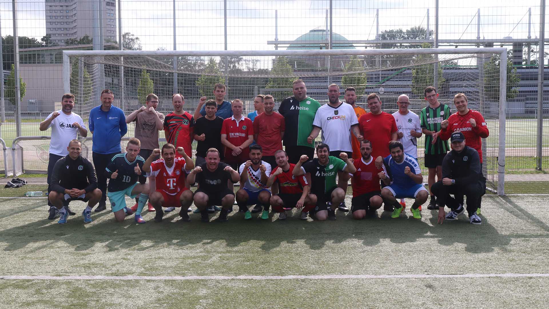 Eine Gruppe von etwas mehr als zwanzig Personen steht auf einem Fußballplatz und jubelt. 