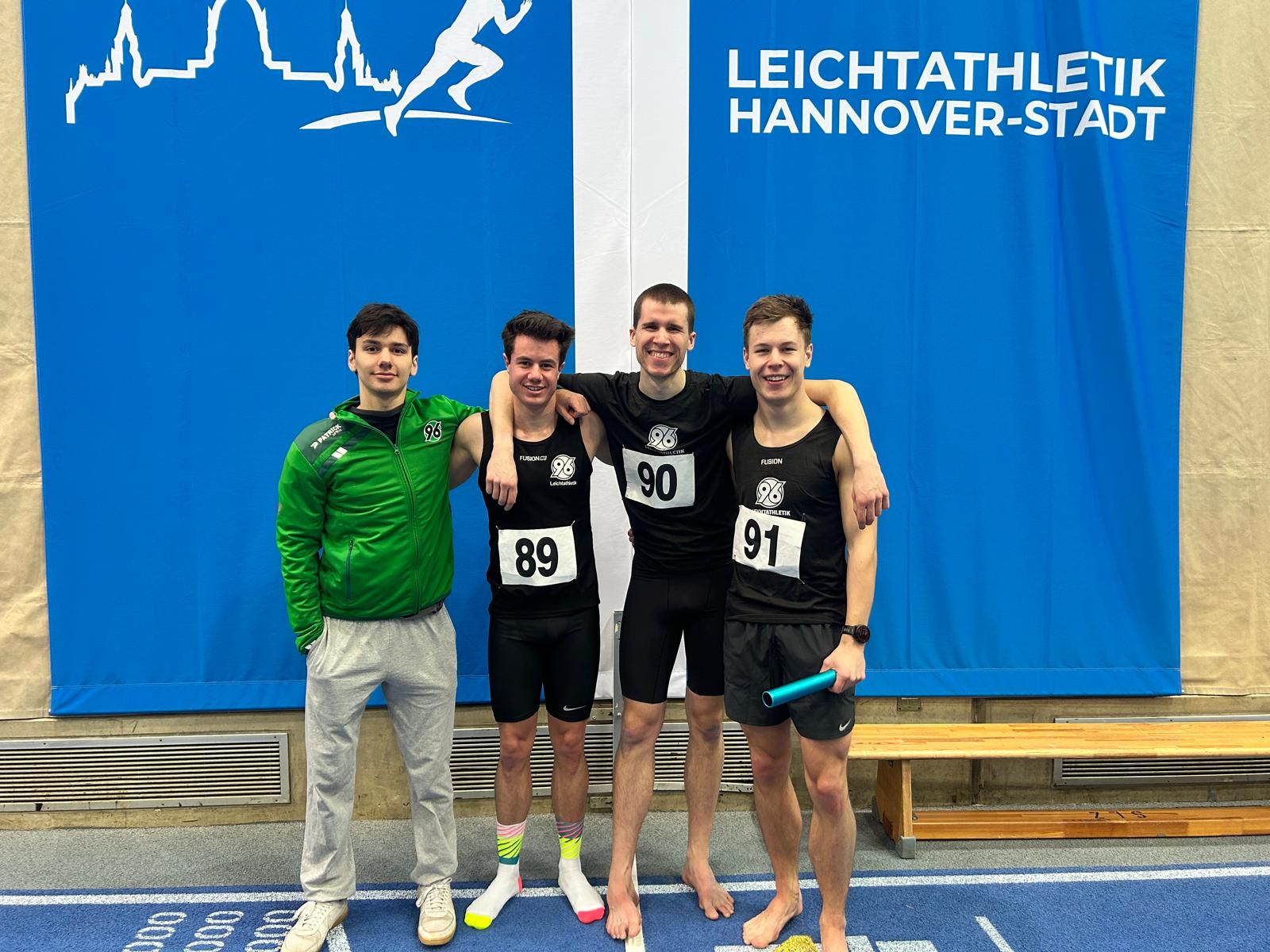 Vier Läufer lächeln mit dem Staffelstab in der Hand in die Kamera.