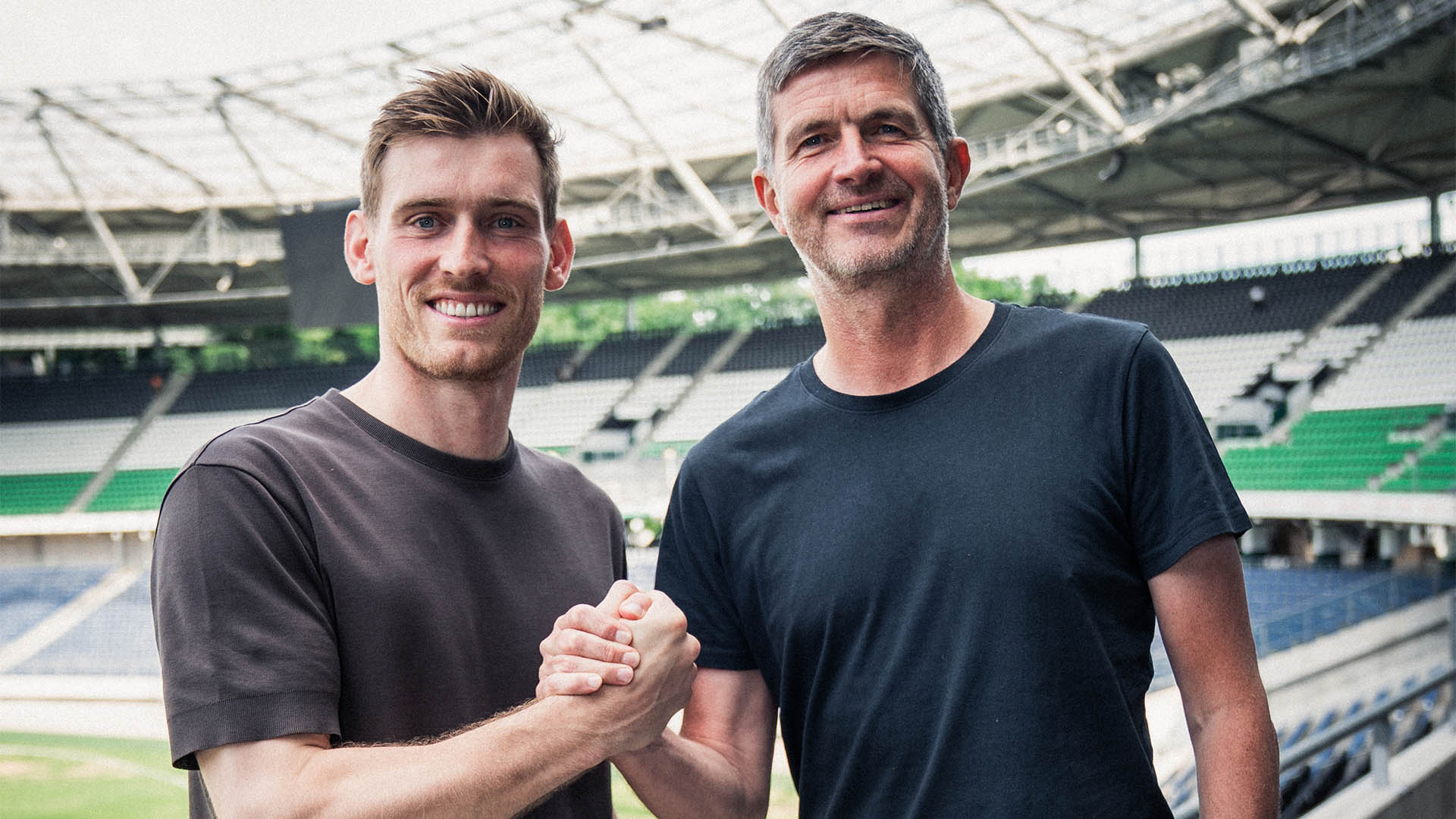 Leo Weinkauf und Ralf Becker beim Handshake im Stadion, dahinter die schwarz-weiß-grüne Nordtribüne.