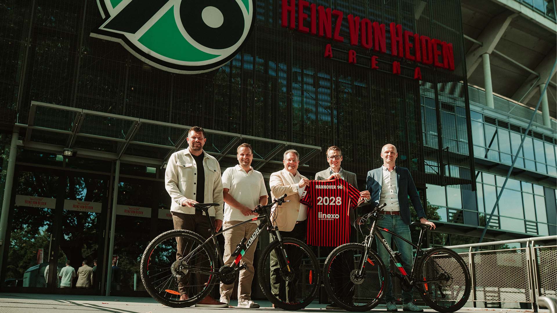 Fünf Personen stehen mit zwei Fahrrädern vor der Heinz von Heiden Arena.