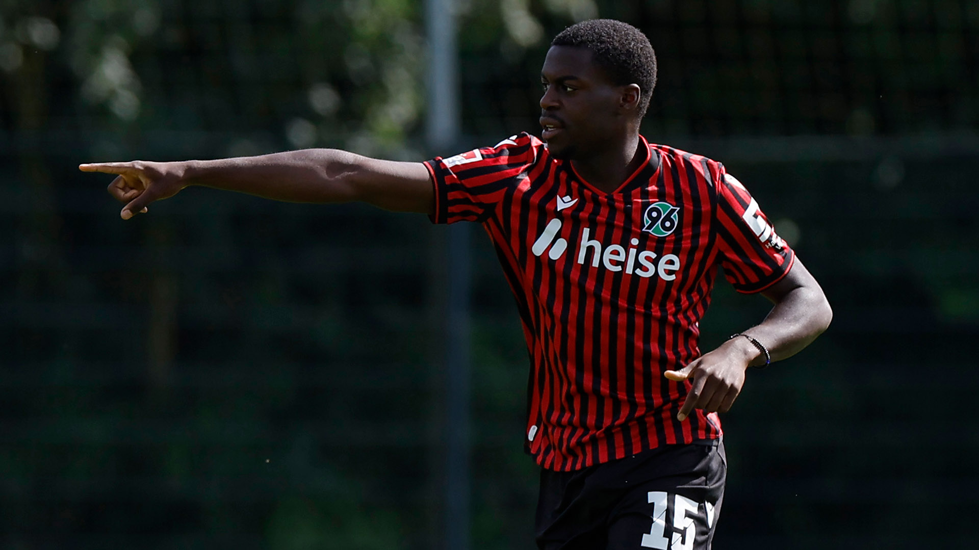 Noel Aseko im Heimtrikot schaut und zeigt nach rechts.