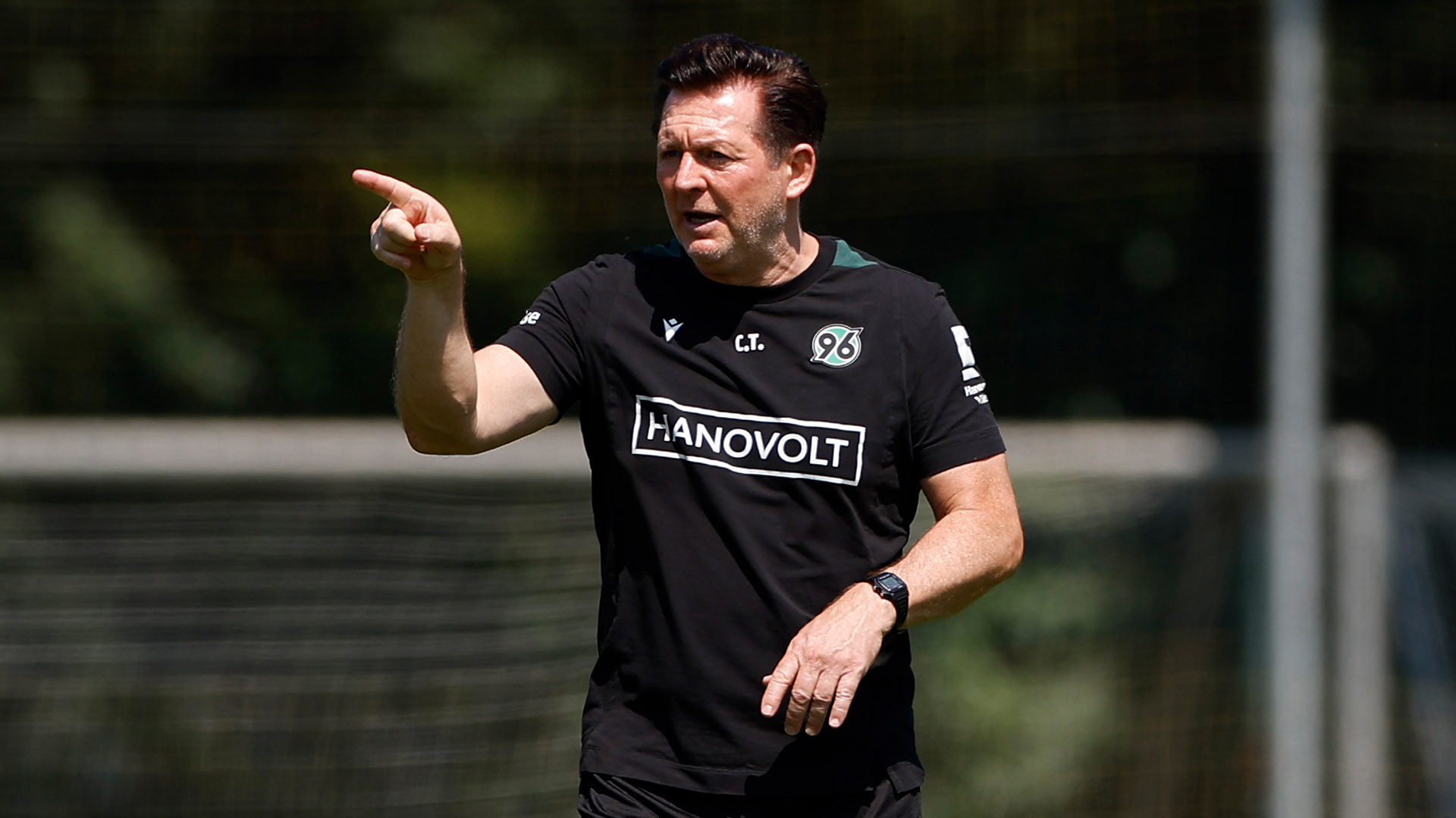 96-Trainer Christian Titz steht auf dem Trainingsplatz und deutet mit dem rechten Zeigefinger nach vorne.