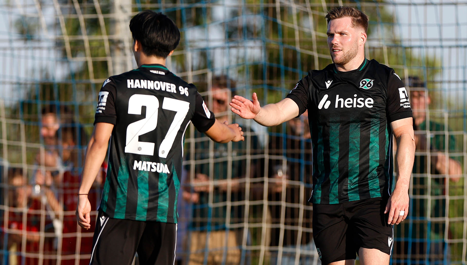 Benjamin Källman ist von vorne zu sehen, er klatscht mit Hayate Matsuda, der von hinten zu sehen ist, ab. Beide tragen das Auswärtstrikot.