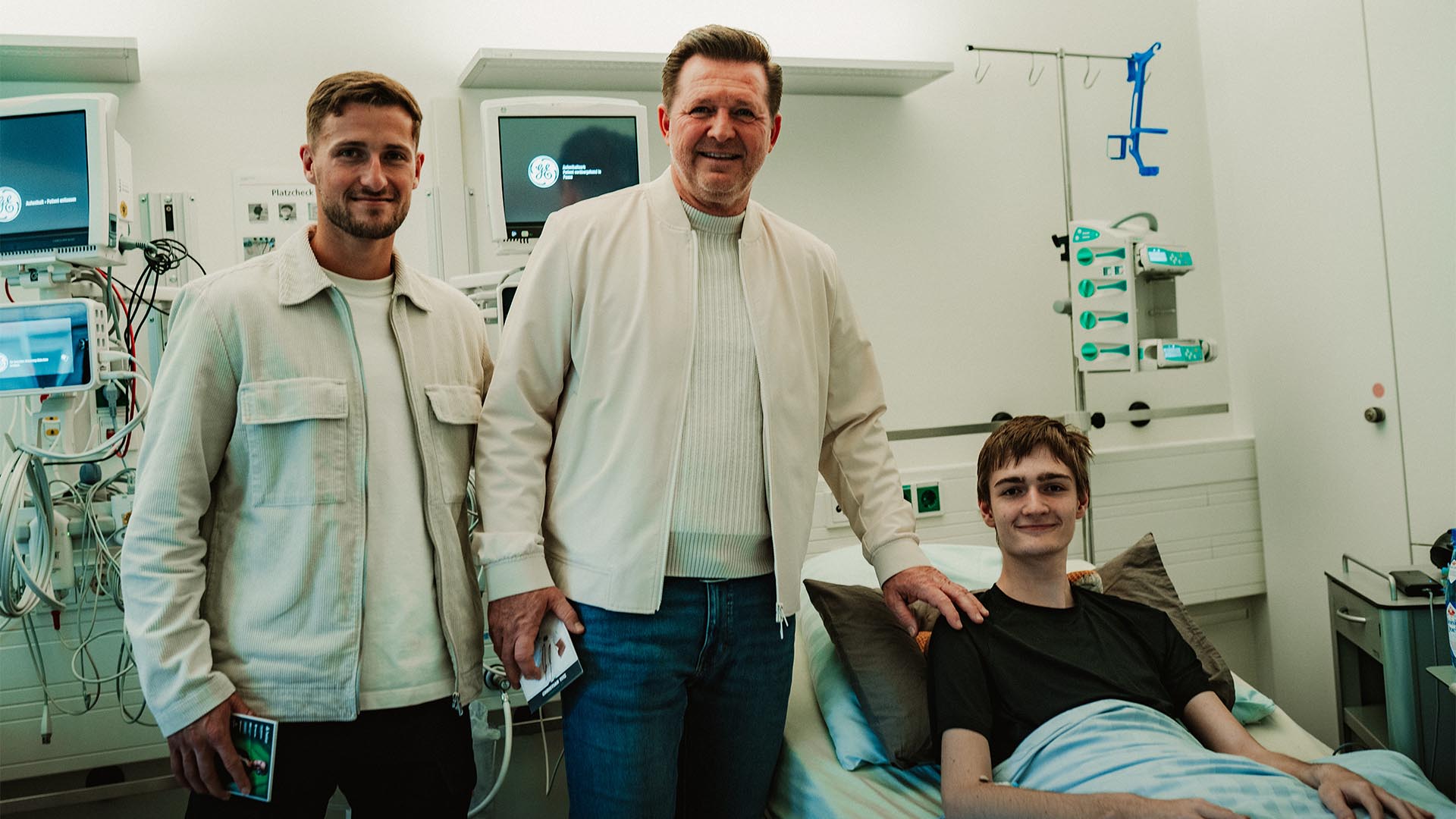 Enzo Leopold und Christian Titz stehen bei einem jungen Patienten am Krankenhausbett.