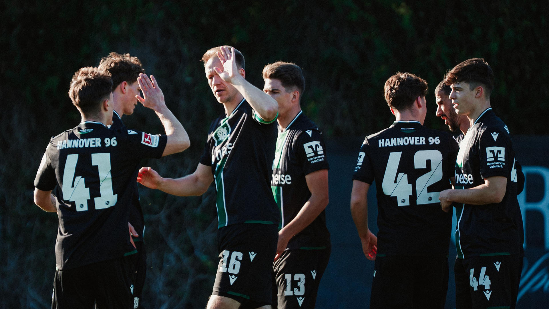 Mehrere Fußballspieler von Hannover 96 in schwarzen Trikots stehen auf dem Spielfeld und klatschen sich nach einem Tor gegenseitig ab.