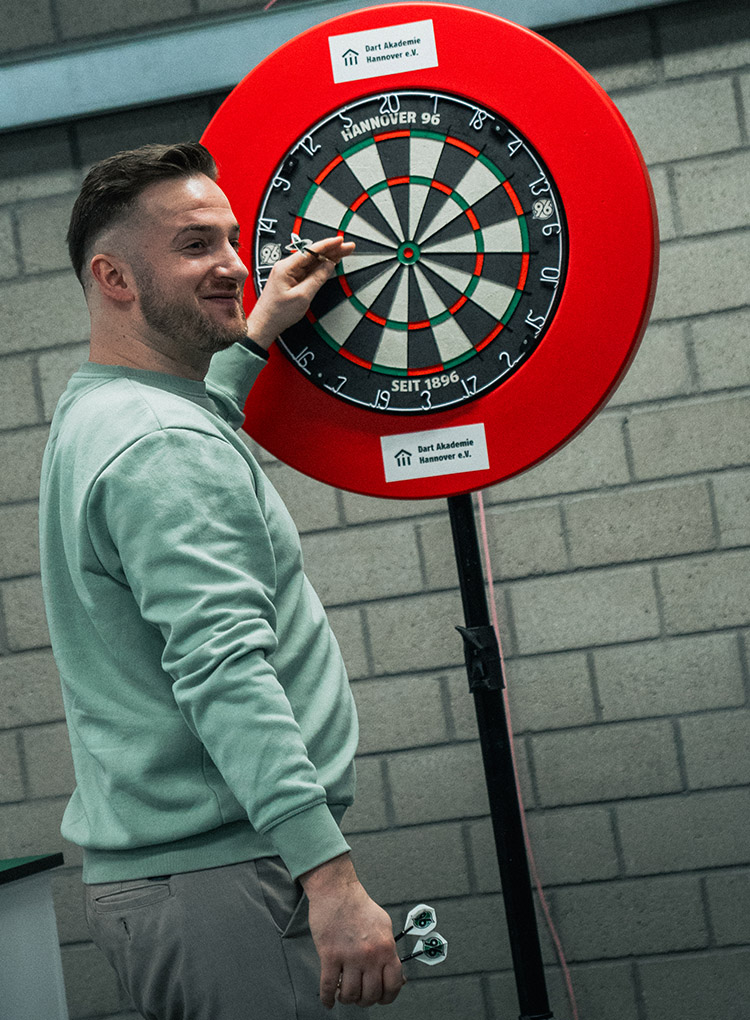 Arno Merk steht an der Dartsscheibe und zieht den Pfeil aus der Triple Elf.