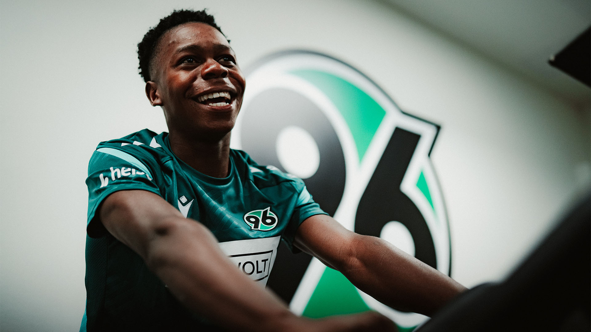 Mwisho Mhango sitzt in Trainingskleidung auf einem Ergometer und strahlt.