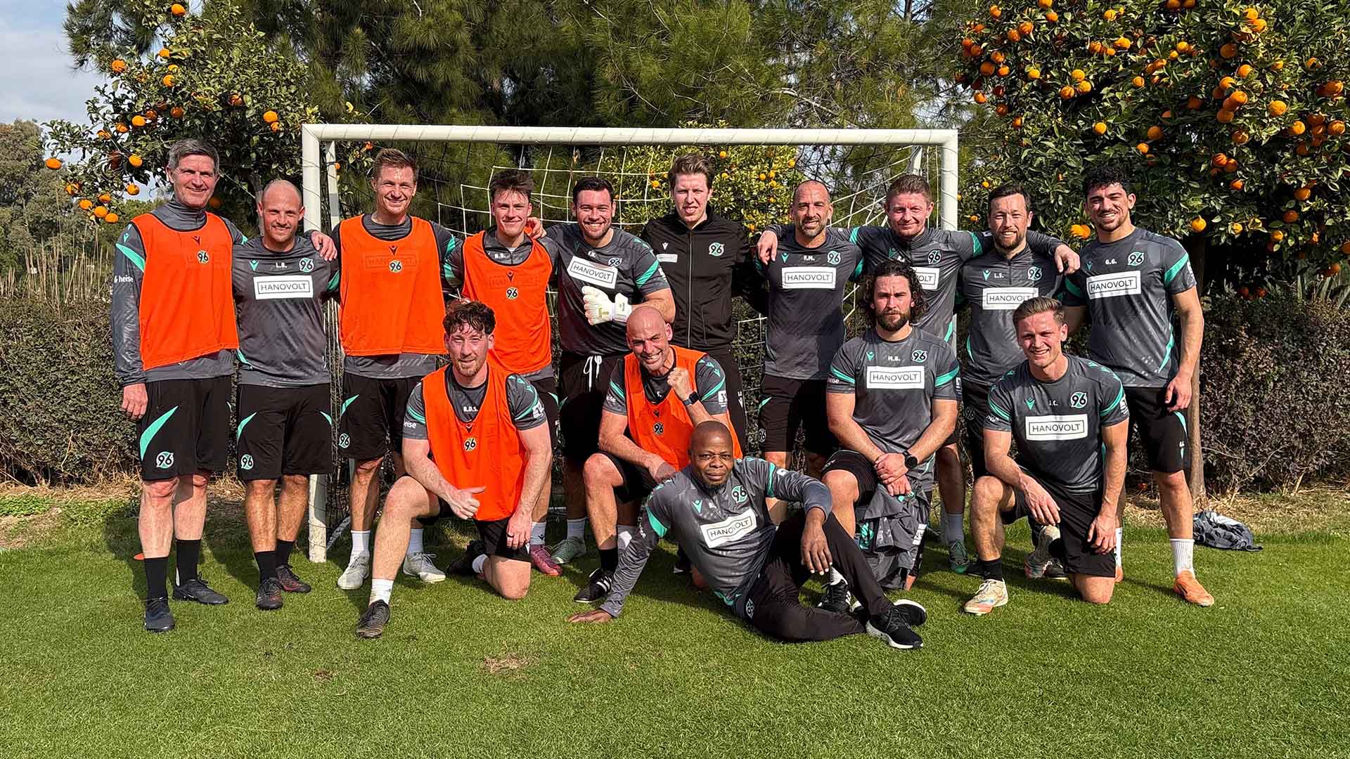 Die Teilnehmer des Mitarbeiter-Kicks posieren nach dem Spiel alle gemeinsam vor einem Tor und Orangenbäumen.