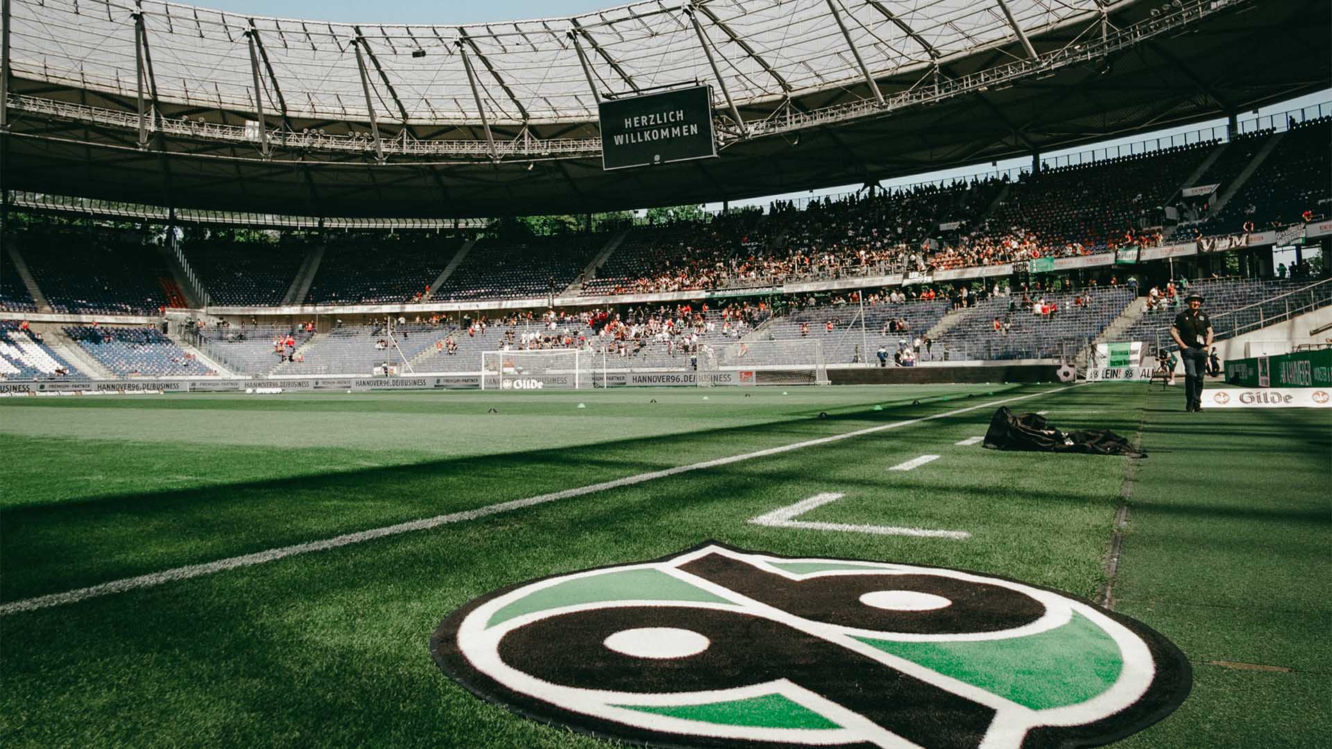 Blick auf die leicht gefüllte Nordkurve des Stadions, im Vordergrund liegt ein 96-Logo-Teppich.