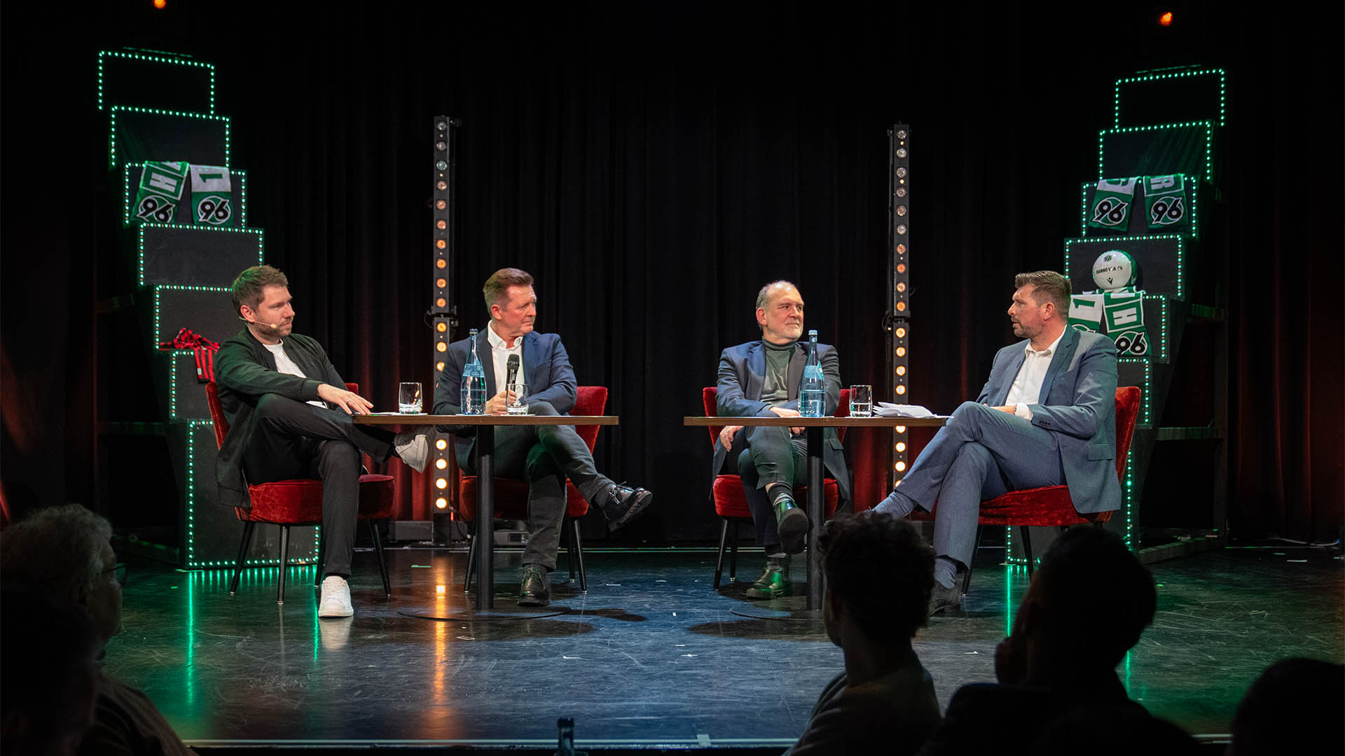 Moderator Christoph Heckmann, Christian Titz, Jörg Schmadtke und Sportfive-Chef Christian Woike sitzen auf roten Sesseln auf einer Bühne und sprechen miteinander. 