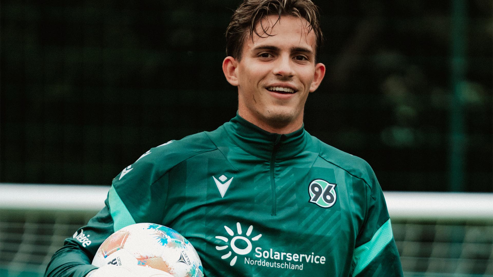 Hannover-96-Neuzugang Nahuel Noll steht im 96-Trainingsoutfit vor dem Tor und hält unter dem rechten Arm einen Ball.