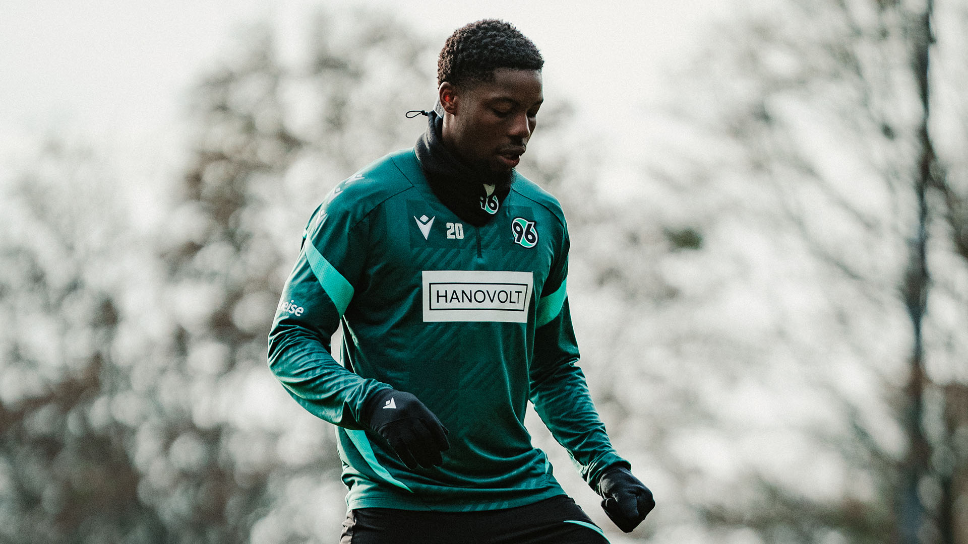 Ime Okon kontrolliert im Training den Ball mit dem Fuß. Er trägt einen grünen Trainingspullover und blickt nach unten auf den Ball.