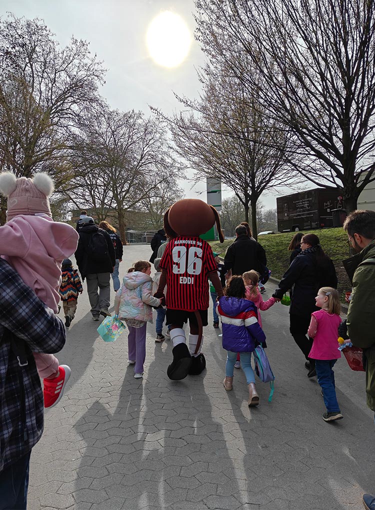Die Kids sind von hinten zu sehen, sie laufen einen Weg entlang, ein Kind ist an der Hand von EDDI.