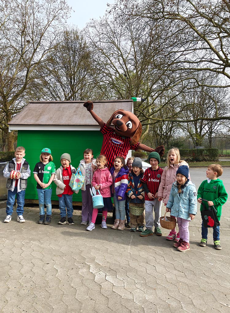 Eine Gruppe von Kindern steht mit EDDI vor dessen grüner Hundehütte am Stadion.