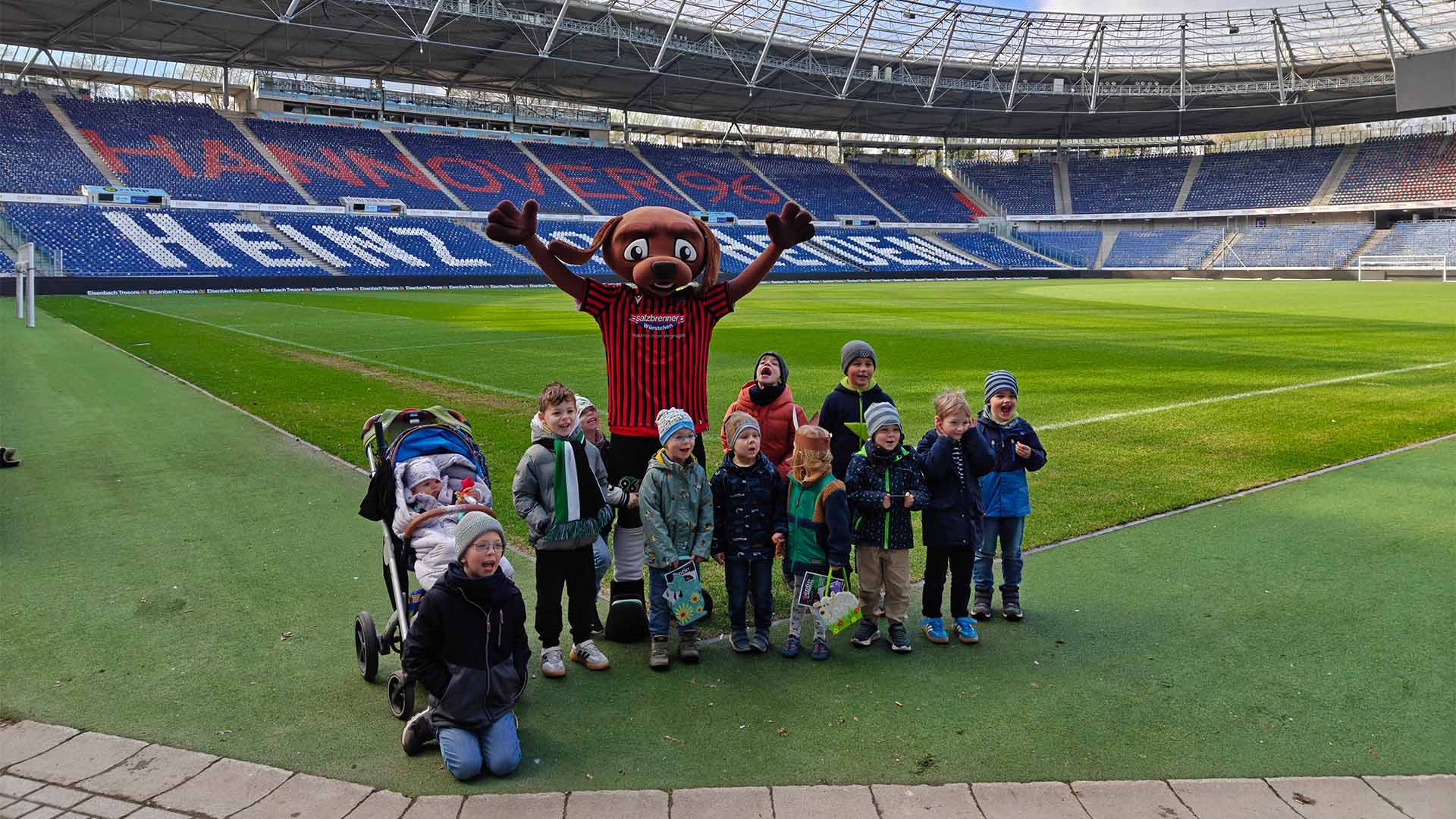 Die Kindergruppe posiert mit EDDI im Stadion, im Hintergrund die leeren Ränge.
