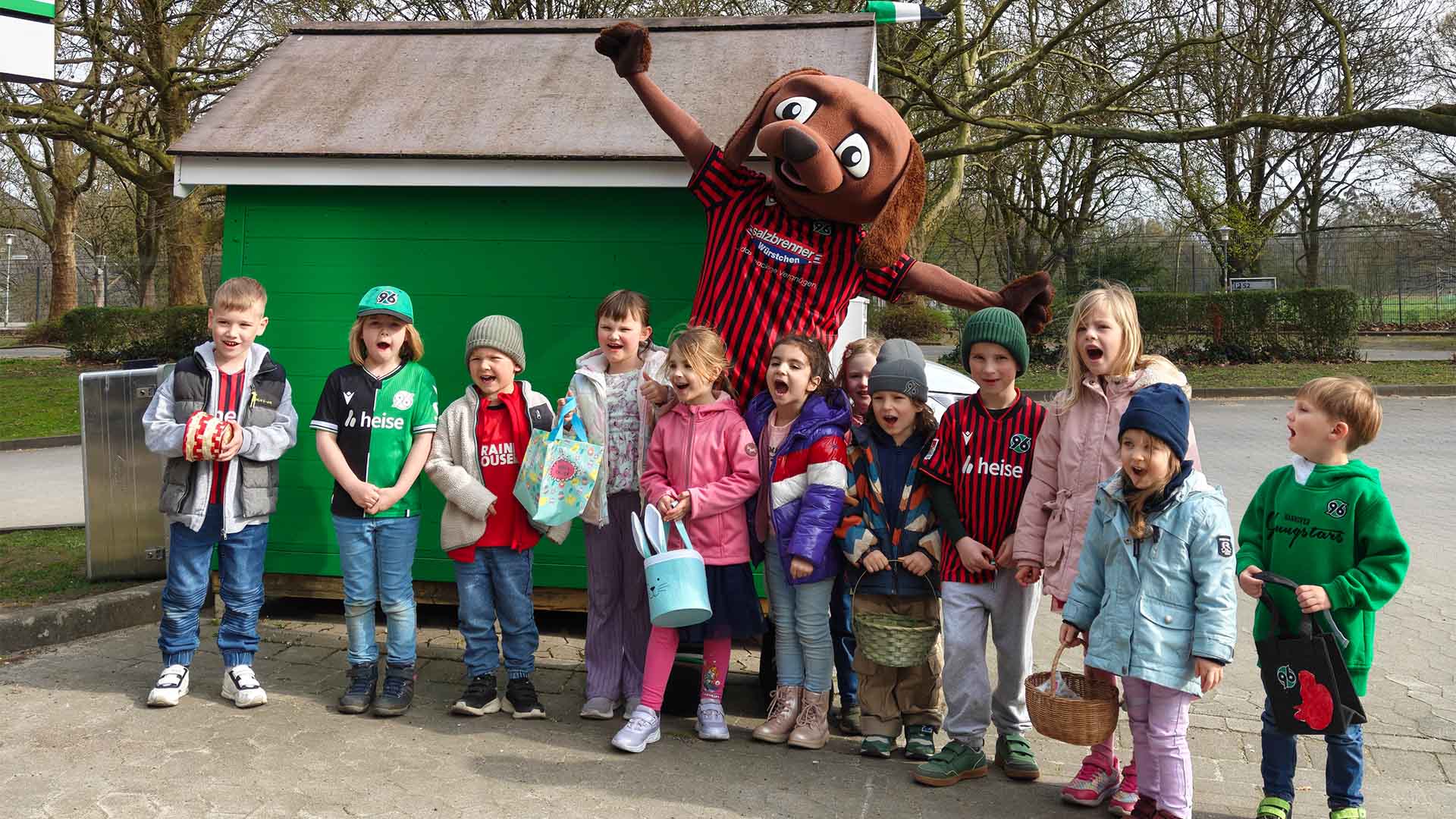 Eine Gruppe von Kindern steht mit EDDI vor dessen grüner Hundehütte am Stadion.