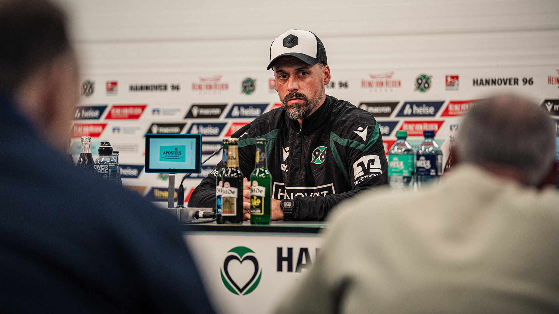 Der 96-Cheftrainer Sandro Wagner sitzt auf dem Pressekonferenz-Podium, im Hintergrund eine Sponsorenwand.