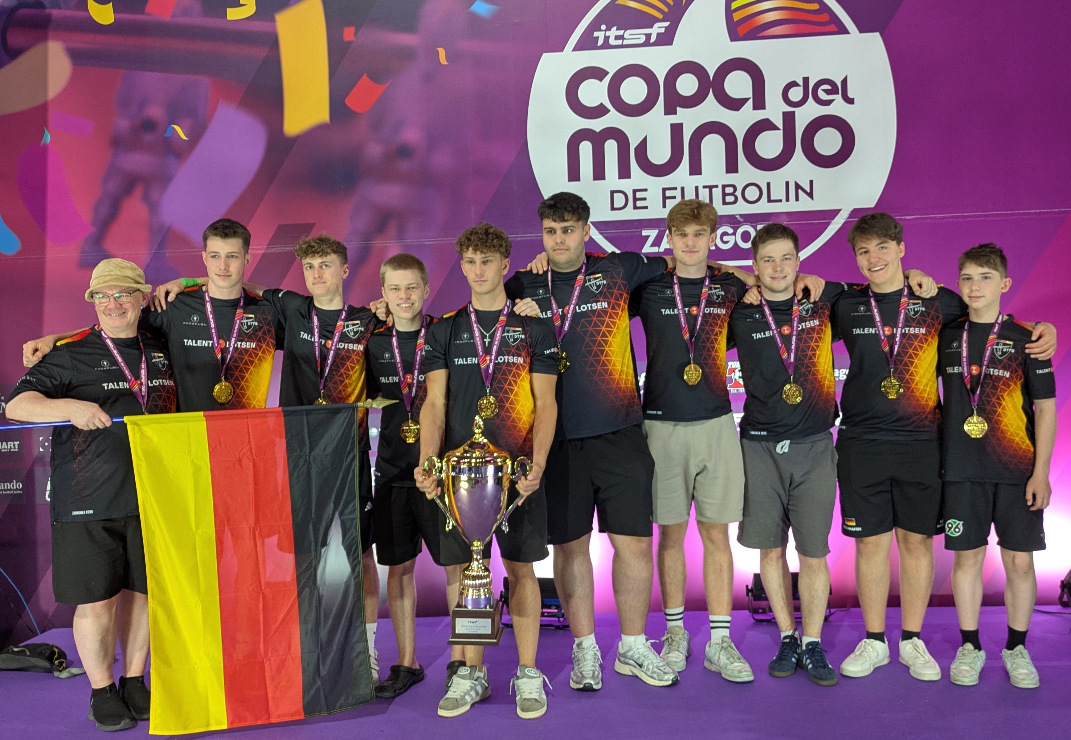 Die Teilnehmer der deutschen Juniorenmannschaft stehen Arm in Arm und freuen sich mit dem Pokal über den Weltmeistertitel.