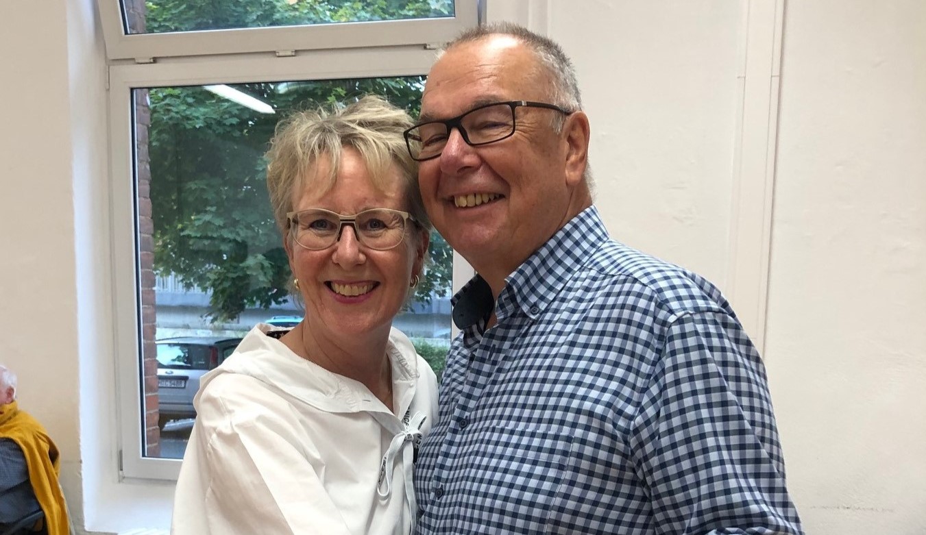 Zwei Personen halten sich Hand an Hand und lächeln in die Kamera.