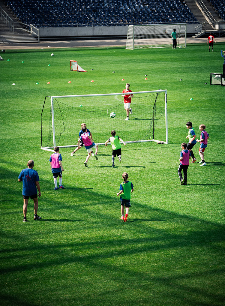 Einige Kinder spielen Fußball auf dem Rasen, ein Tor steht in der Mitte.