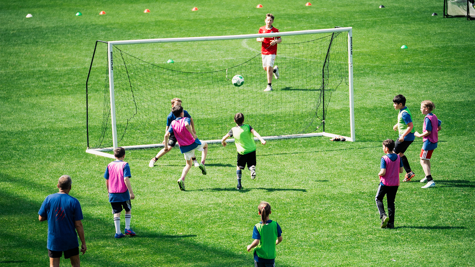 Einige Kinder spielen Fußball auf dem Rasen, ein Tor steht in der Mitte.