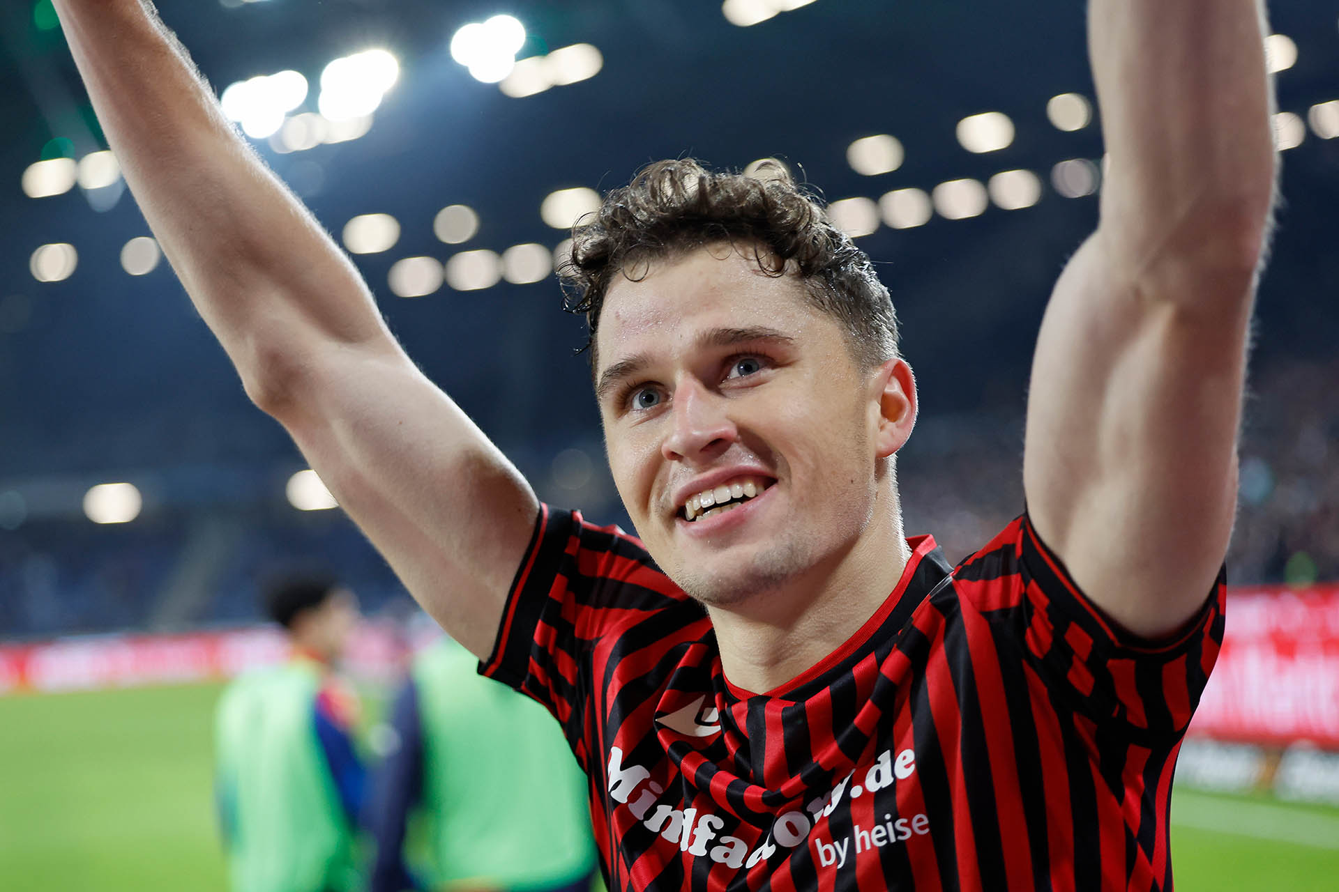 Benedikt Pichler hebt lächelnd die Arme und schaut in Richtung Fans. 