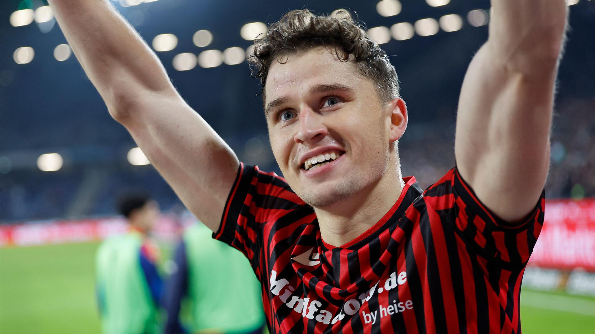 Benedikt Pichler hebt lächelnd die Arme und schaut in Richtung Fans. 