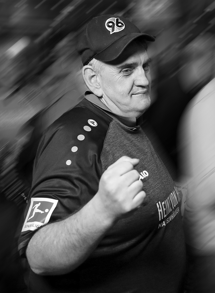 Schwarz-weißes Bild von 96-Fan Popcorn-Olaf in einem älteren 96-Trikot und mit 96-Cap.