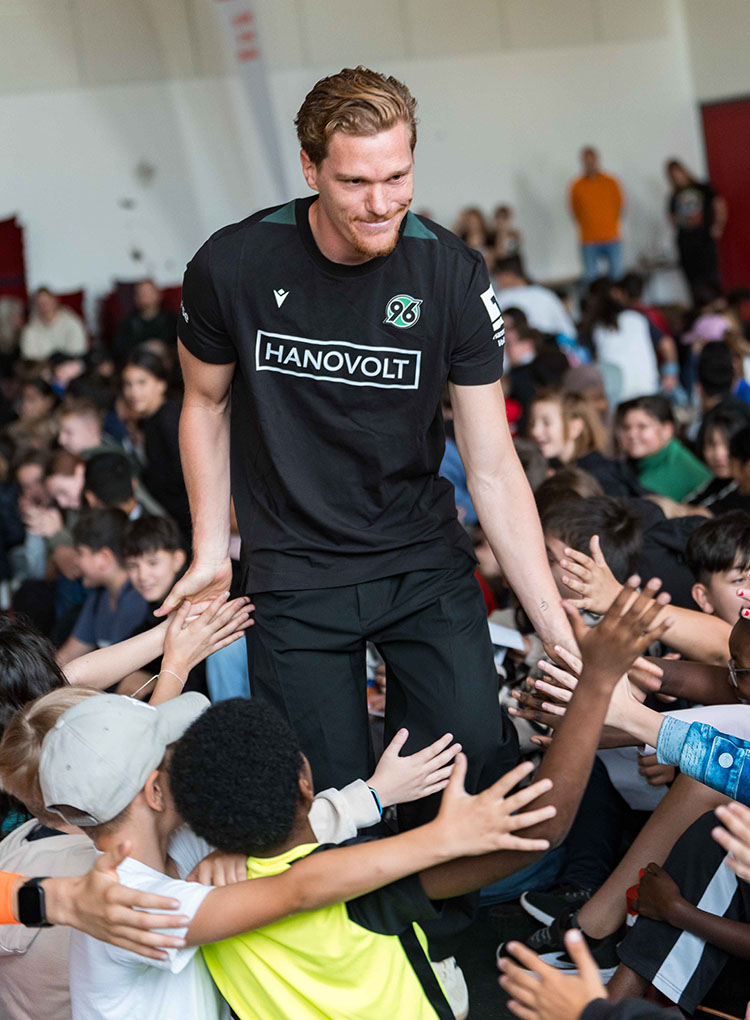 Der ehemalige 96-Profi Marcel Halstenberg läuft in einem schwarzen 96-T-Shirt durch ein Pulk von Kindern und klatscht mit ihnen an. 