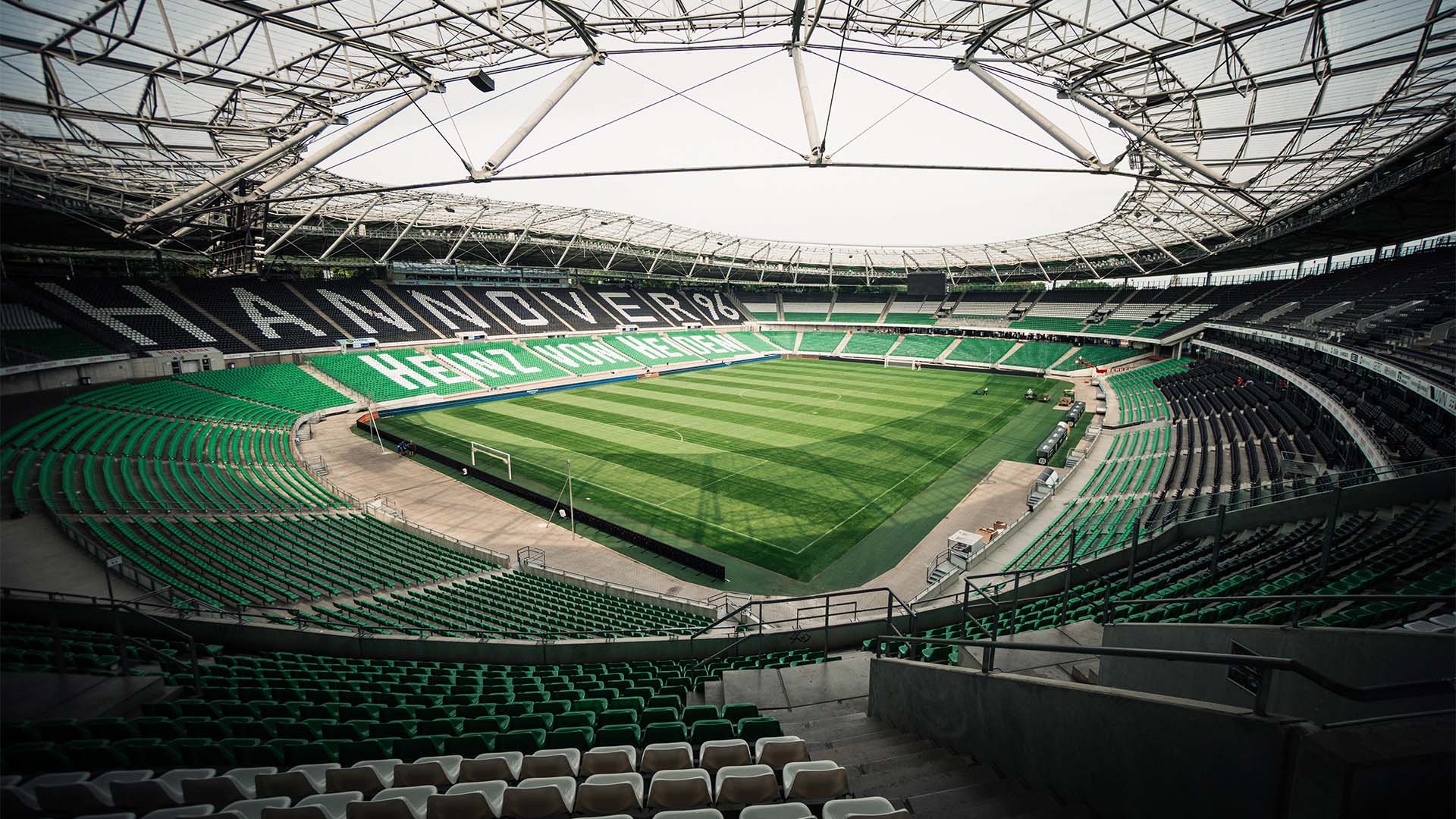 Blick ins leere 96-Stadion mit schwarzen, weißen und grünen Sitzen.