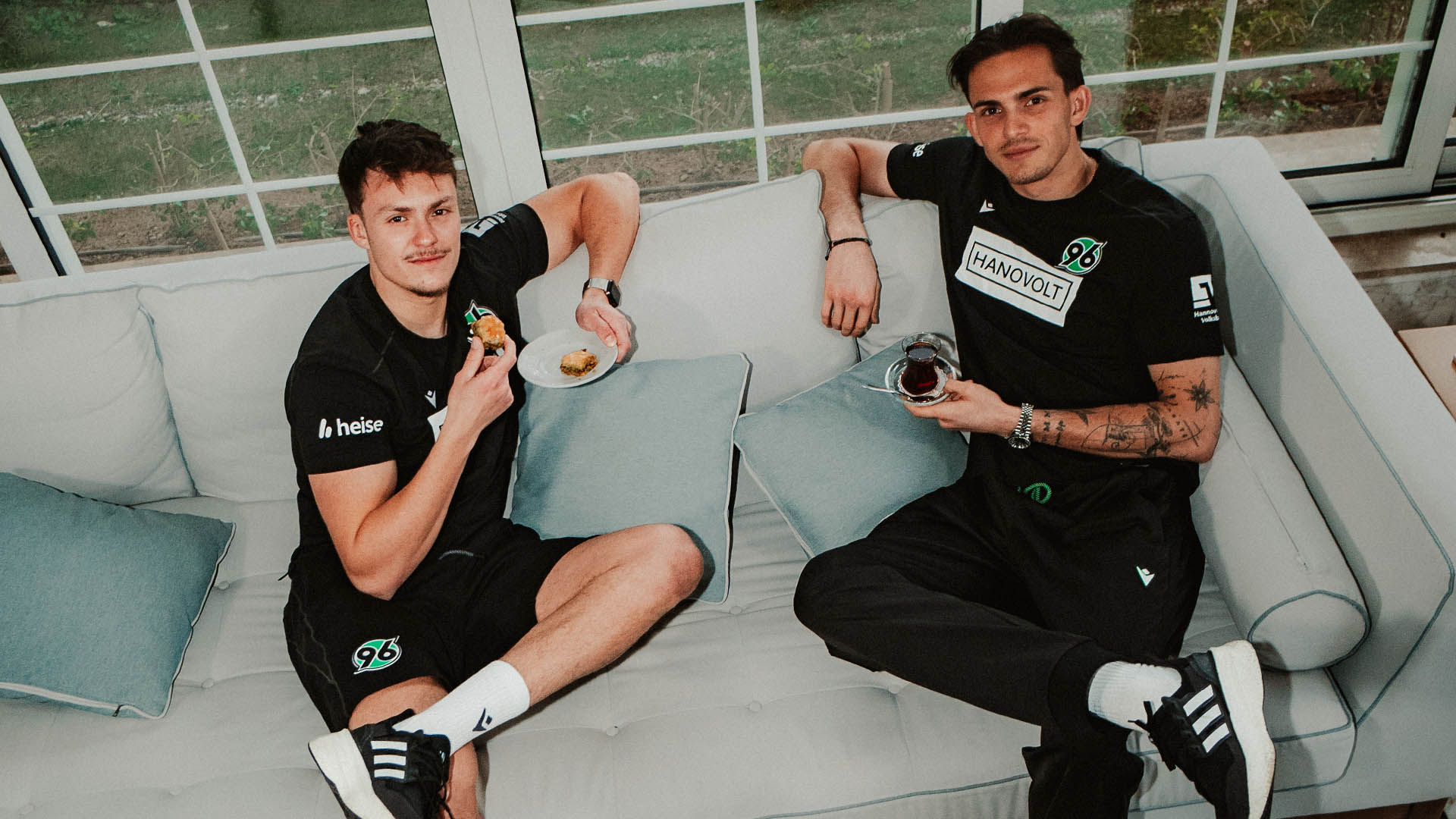 Niklas und Nahuel Noll sitzen auf dem Sofa, mit Baklava und Chai in der Hand.